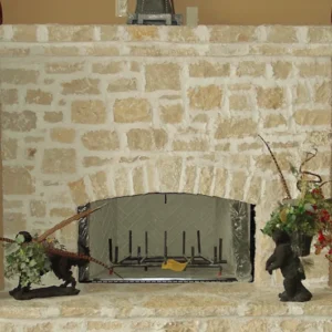 A rustic stone fireplace with a rectangular opening features decorative sculptures on either side. One sculpture depicts a bird with colorful feathers, while the other resembles a small animal. The fireplace interior is empty. StoneSupplyStore.com We Sell Stone, Repair Stone, and Do Stone Projects